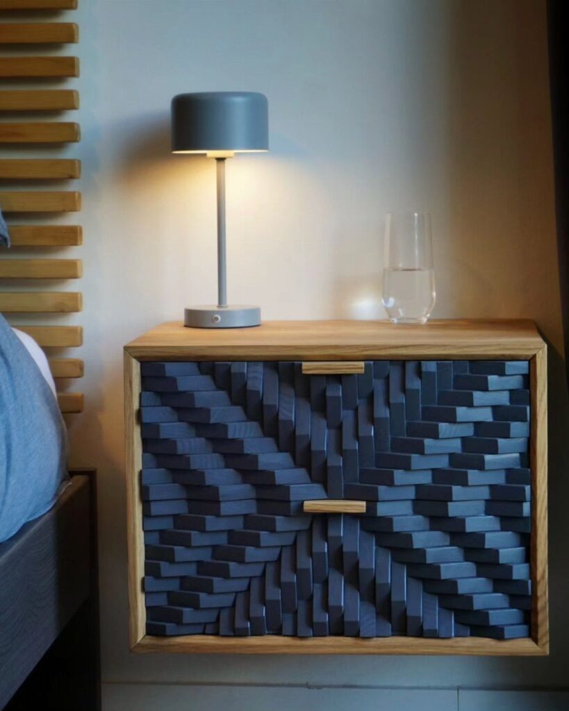 Wooden bedside table with dark blue geometric textured slats and a grey lamp.