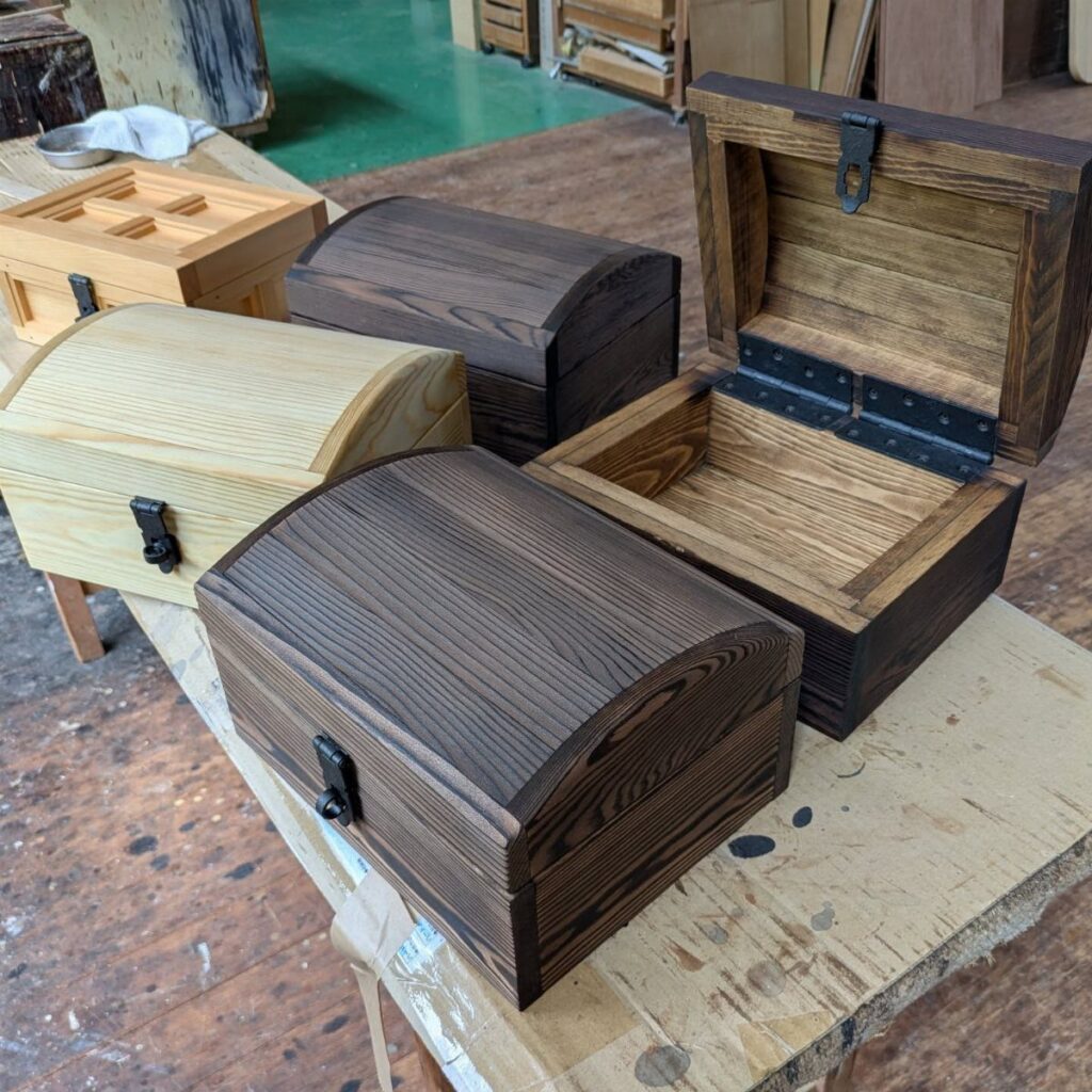 Handmade wooden treasure chests in different stains resting on a workshop workbench.