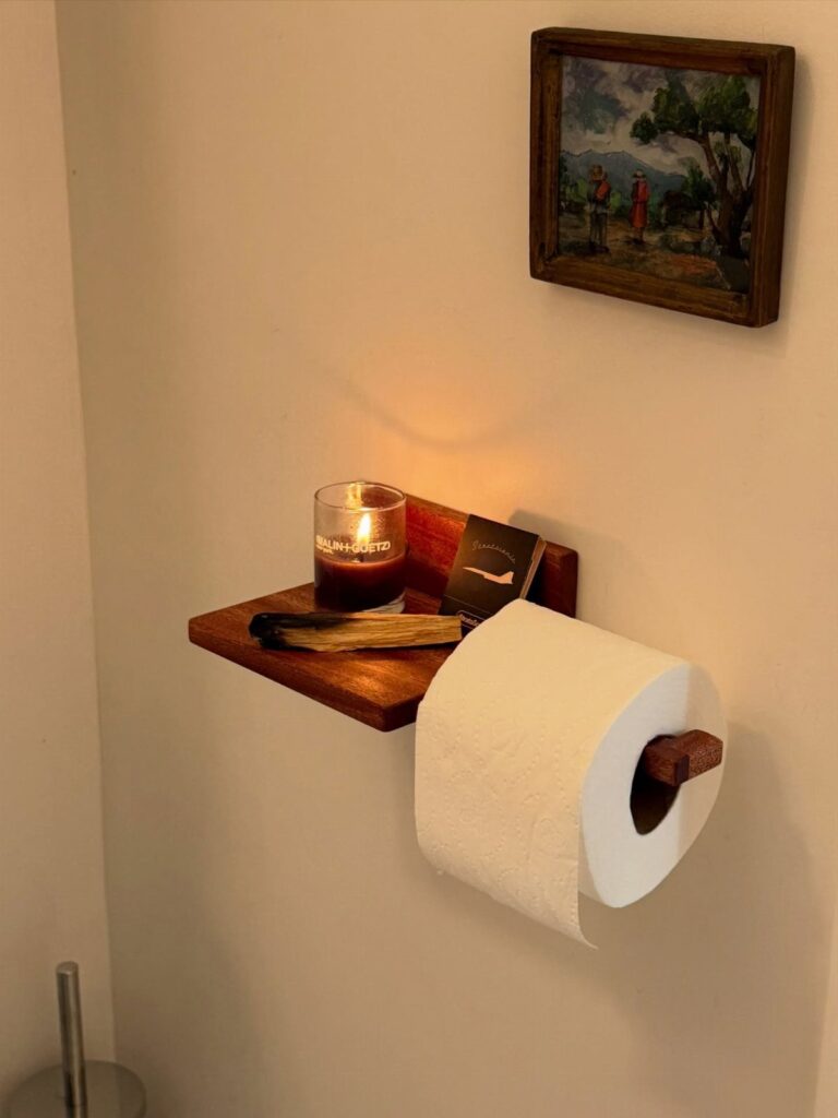 Wooden wall-mounted toilet paper holder with a small shelf and a lit candle.
