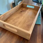 Wooden serving tray with handle cutouts sitting on a dark wood table.