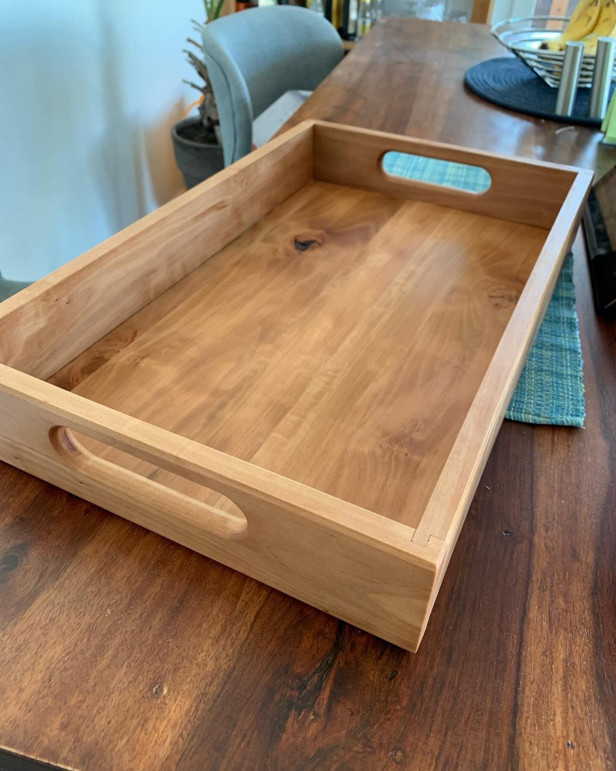 Wooden serving tray with handle cutouts sitting on a dark wood table.