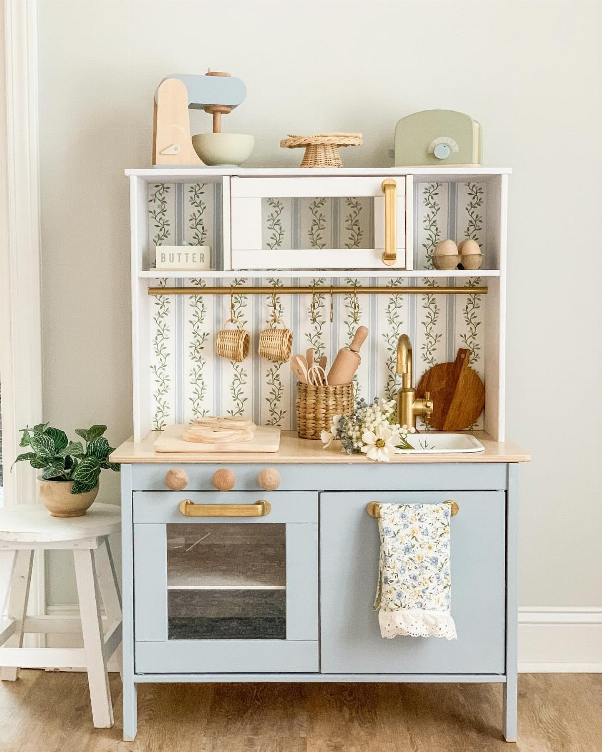 Child's play kitchen made from a repurposed cabinet with light blue paint and floral wallpaper.