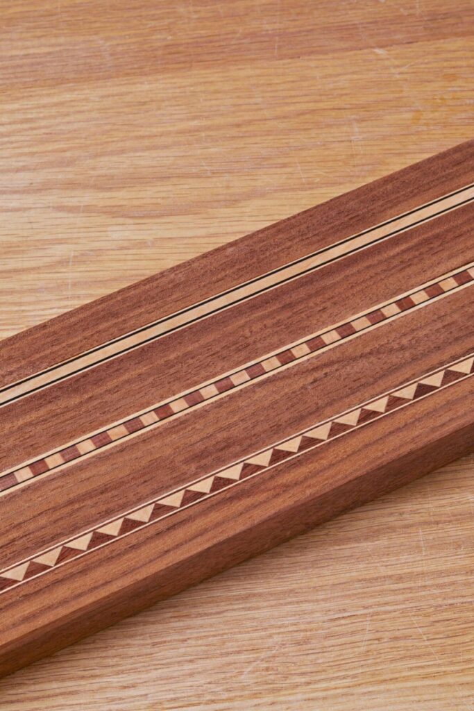 Reddish-brown wooden plank with decorative light-colored linear and triangular wood inlays.