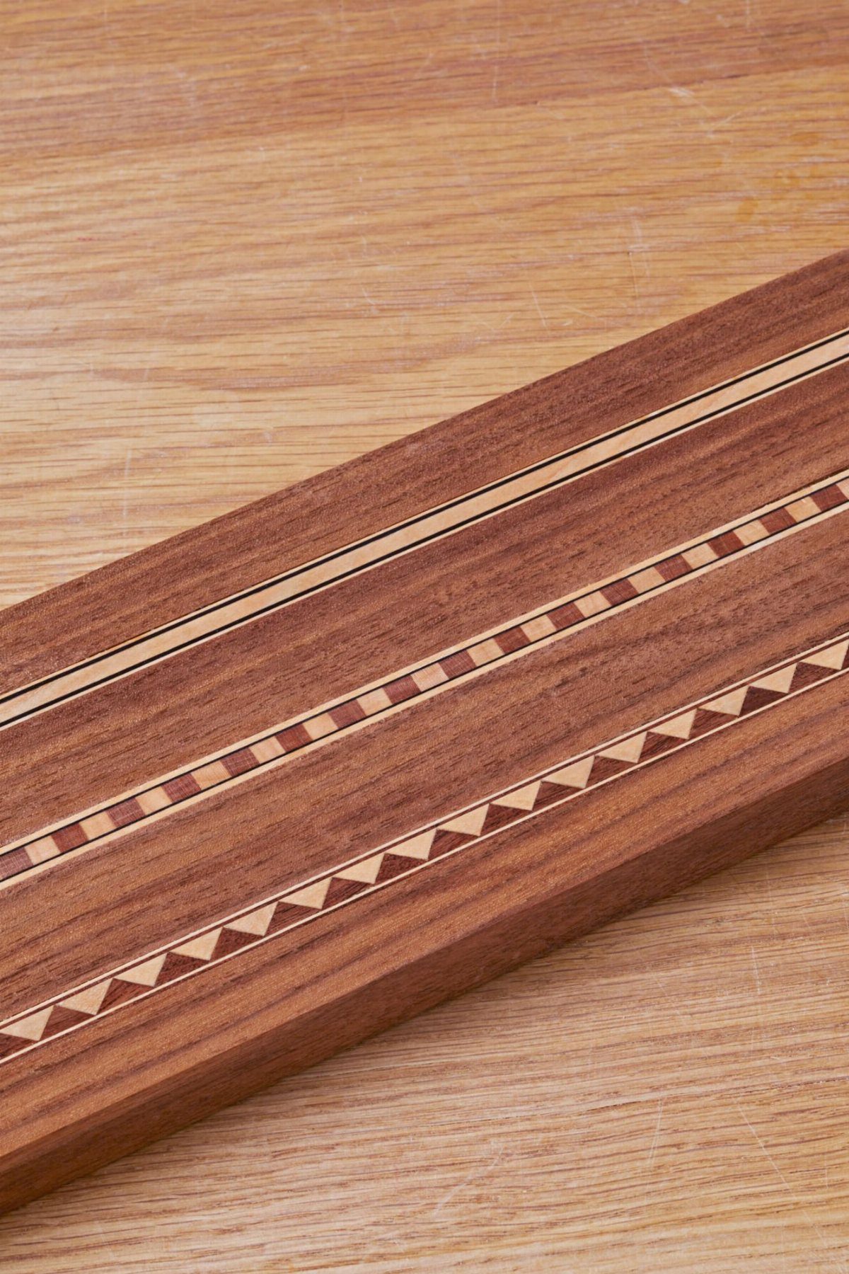 Reddish-brown wooden plank with decorative light-colored linear and triangular wood inlays.