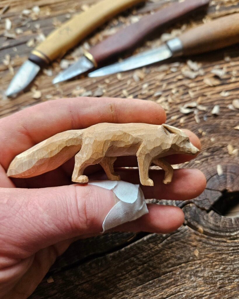 Hand-carved wooden fox figure held above carving tools and wood shavings.