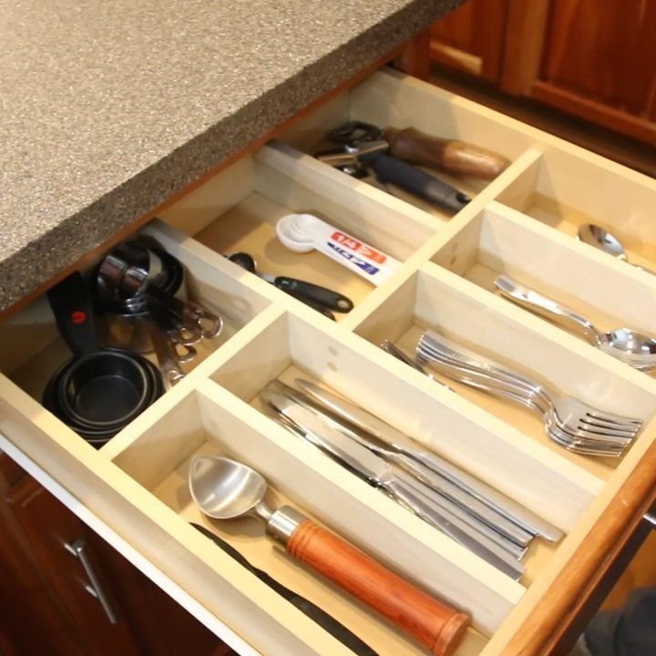Wooden kitchen drawer organizer with custom dividers holding various silver utensils and tools.