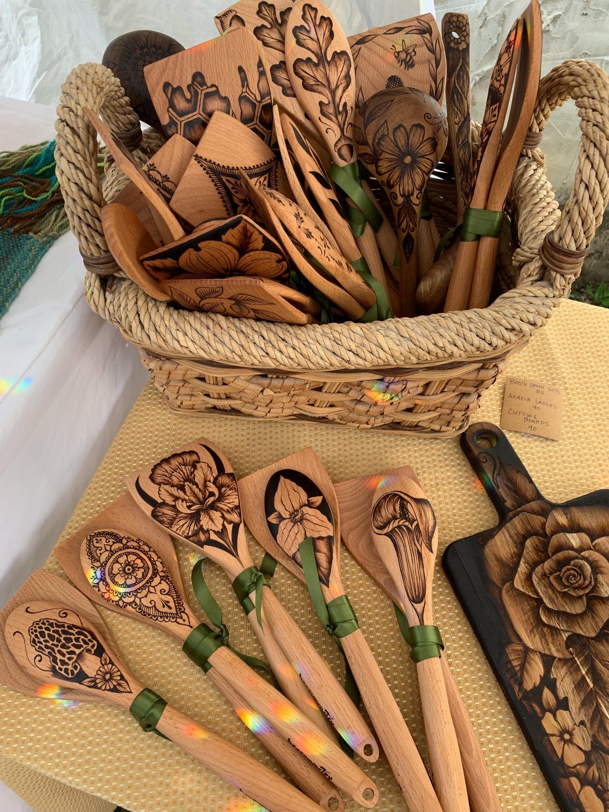 Wood-burned kitchen spoons with floral designs arranged in a basket and on a table.