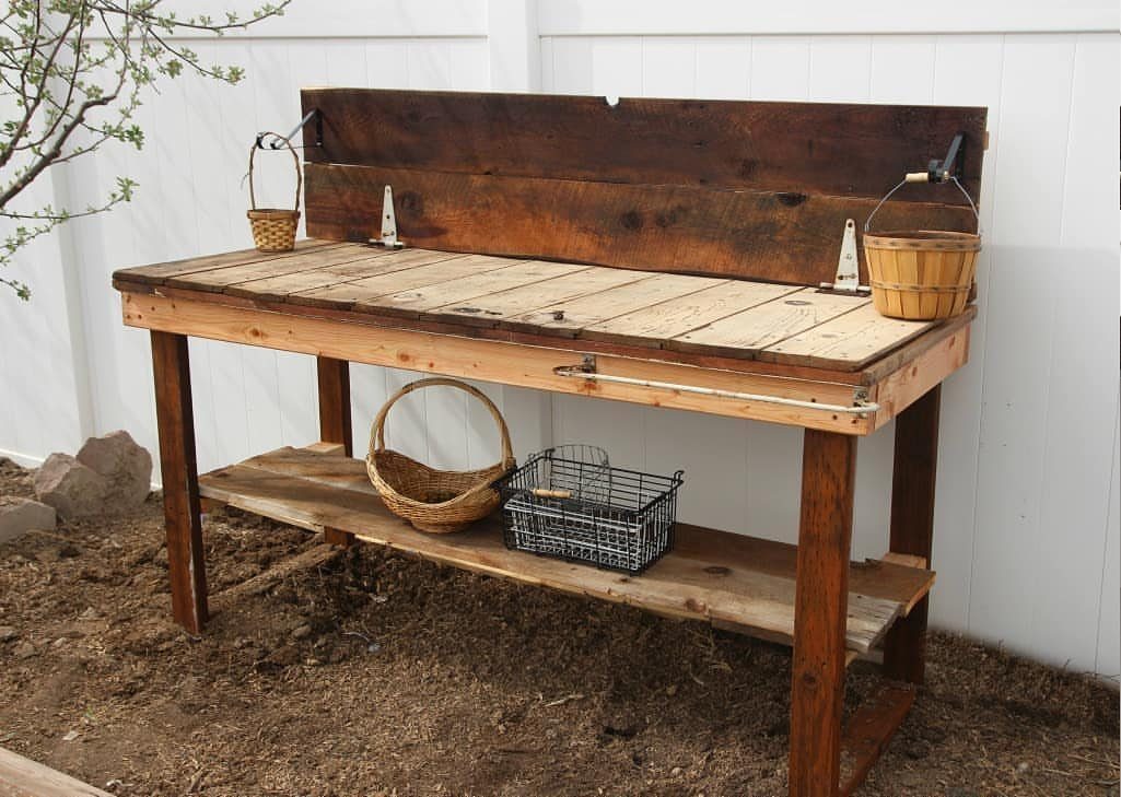 Rustic wooden potting bench with baskets and wire bin against a white fence.