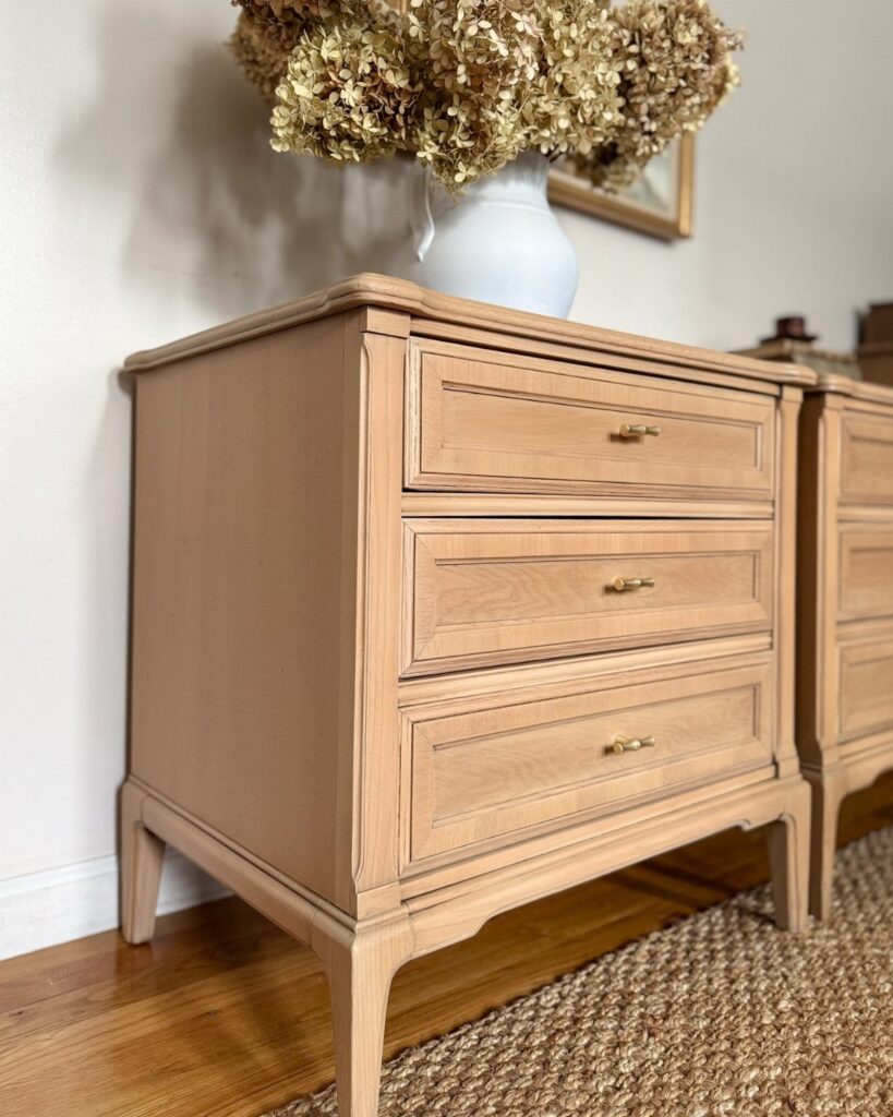 Light-brown wooden dresser with gold handles and dried flowers in a white vase