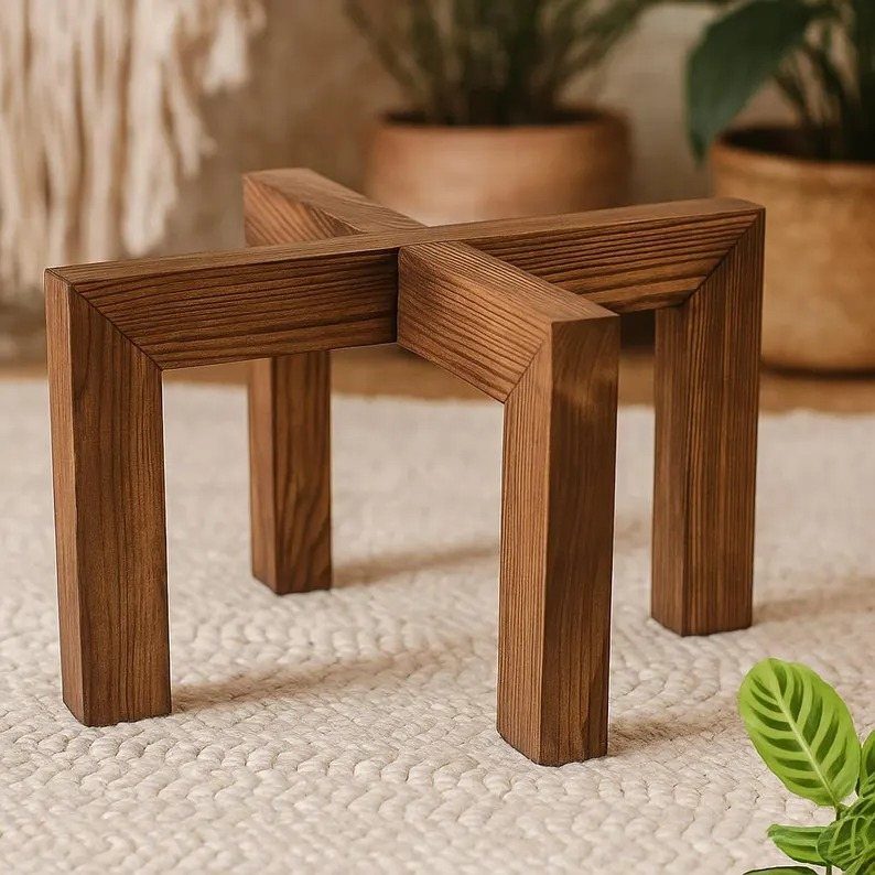 Wooden cross-shaped plant stand resting on a white textured woven rug.
