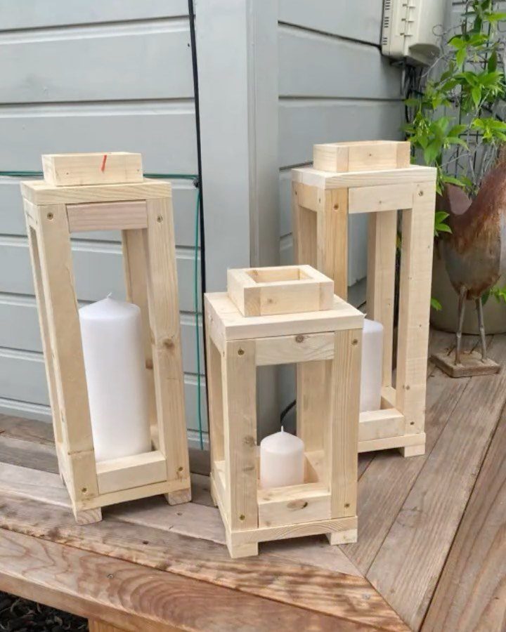 Three rustic wooden lanterns with white pillar candles on a wooden deck.