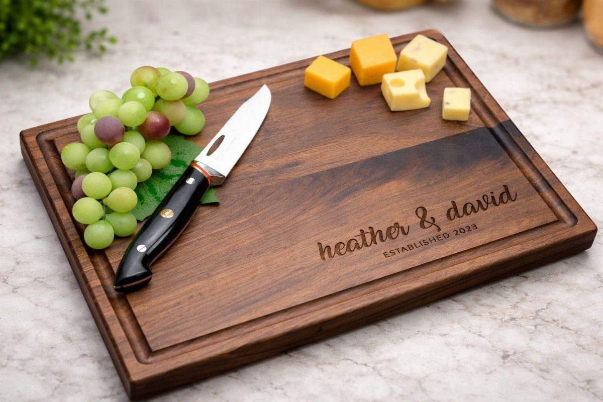 Personalized wooden cutting board with grapes, cheese, and a knife on marble.