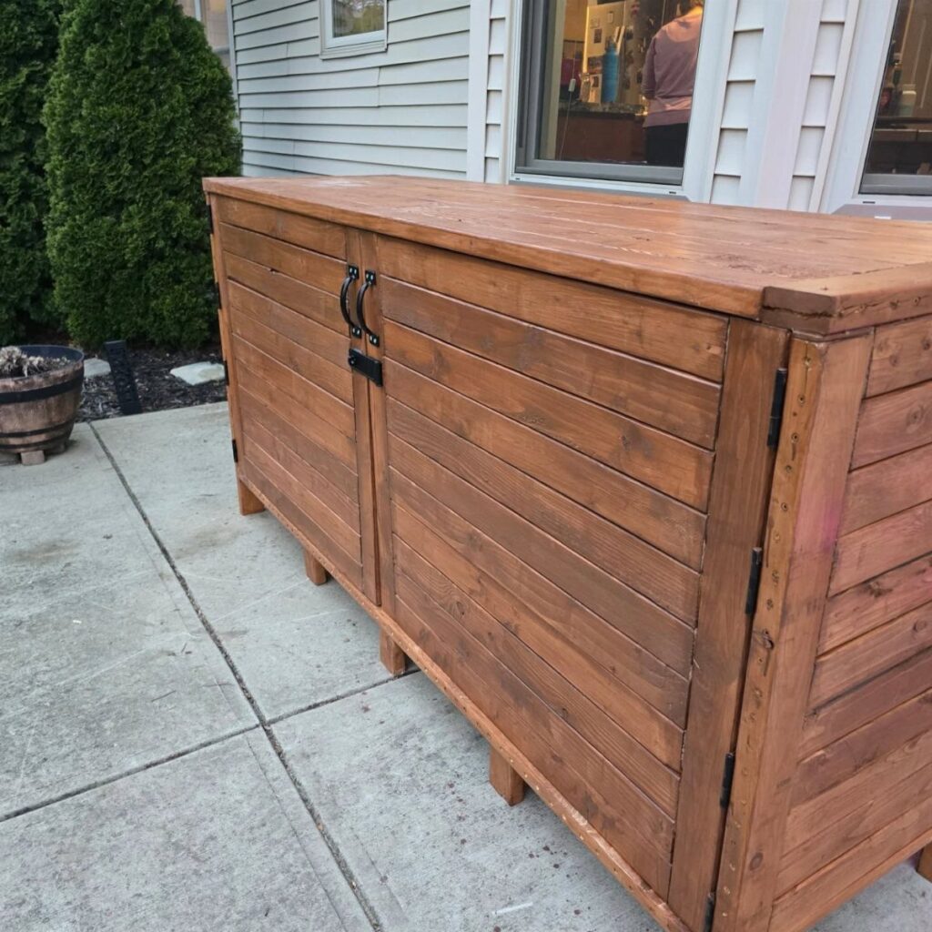 Large brown wooden storage bin with doors sitting on a concrete outdoor patio.