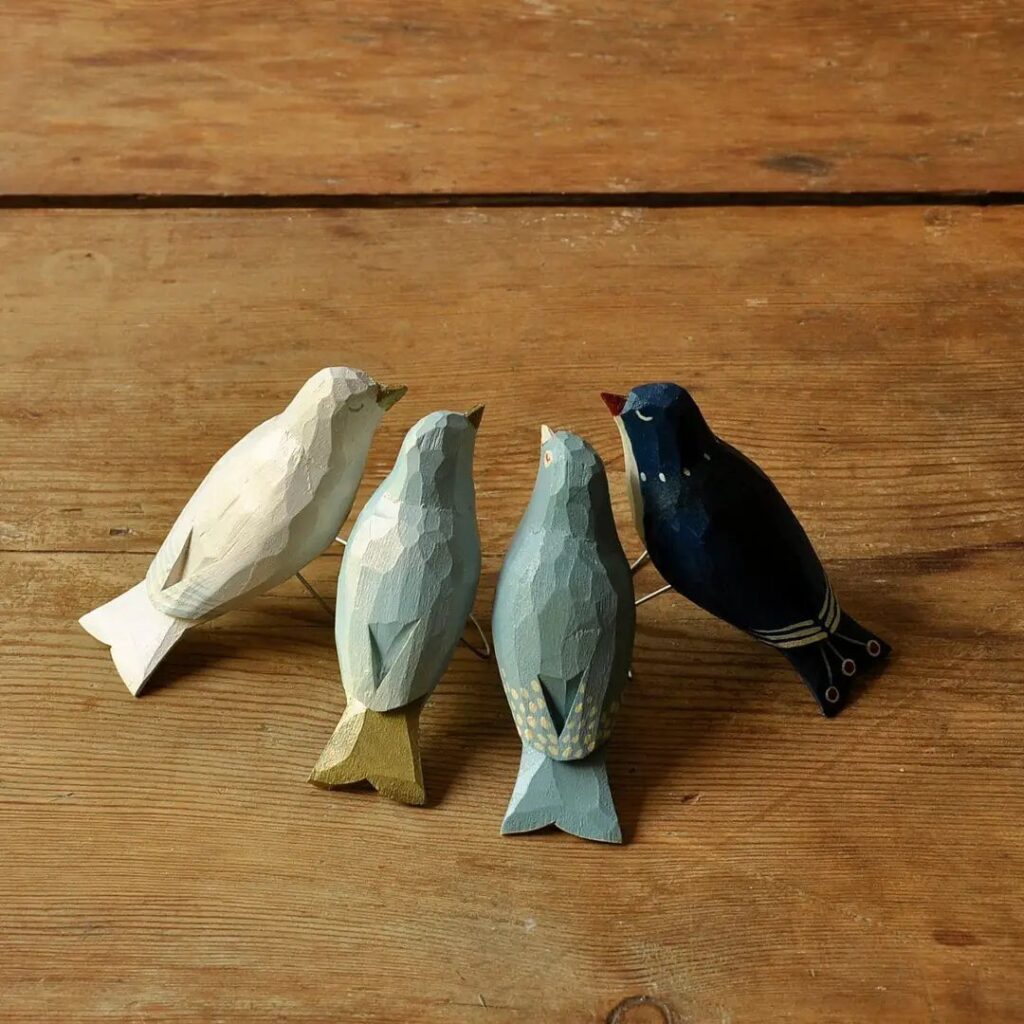 Four faceted hand-carved wooden birds in various colors on a wooden table.