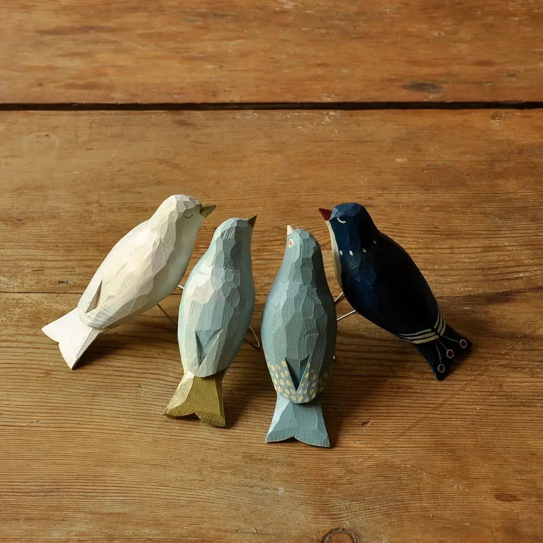 Four faceted hand-carved wooden birds in various colors on a wooden table.
