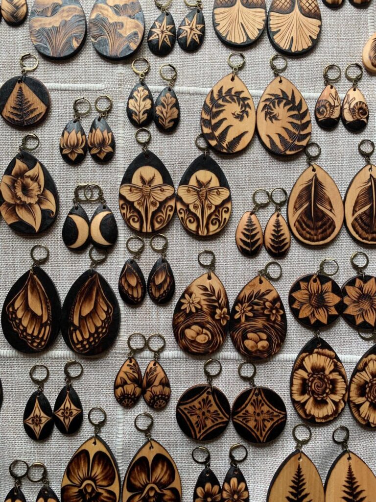 Wooden earrings with intricate wood burned floral and leaf patterns on white fabric.