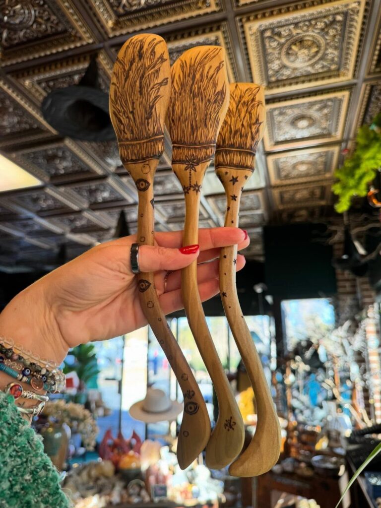 Three wooden spoons with detailed wood-burned wheat and celestial art held by a hand.