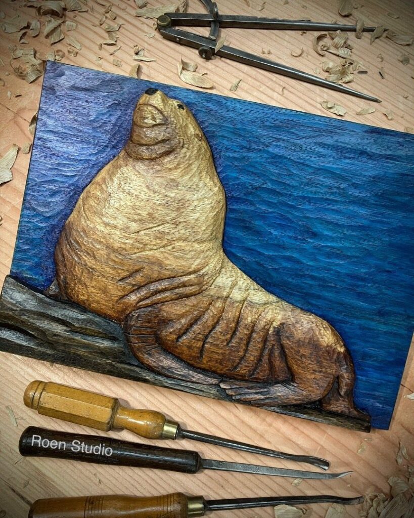 Carved wooden seal resting on a log against a blue background with carving tools.