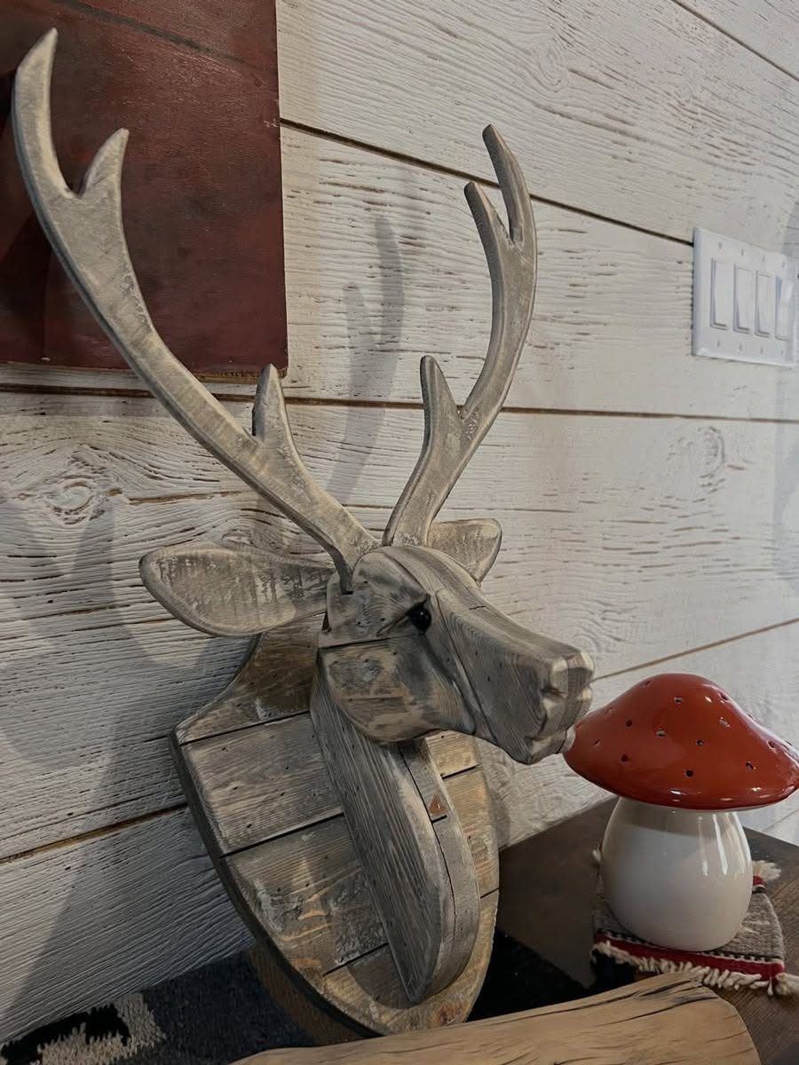Carved wooden deer head mounted on a plaque against a white wooden wall.