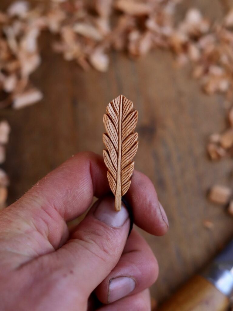 Carved wooden feather held by a hand over a surface of wood shavings.