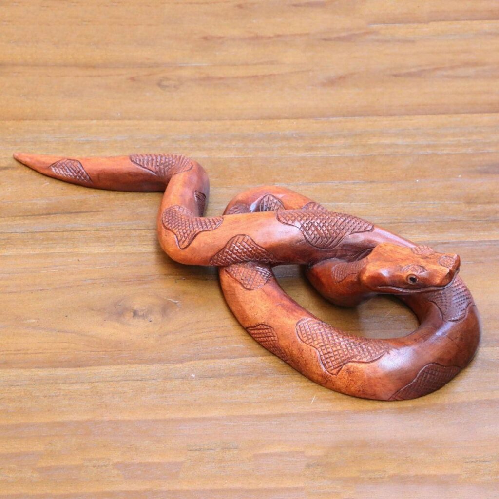 Wooden snake sculpture with detailed scales coiled on a light wood surface.