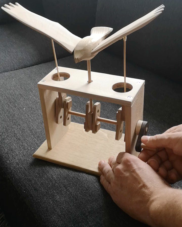 Wooden mechanical bird toy with wings, operated by a hand crank on a frame.