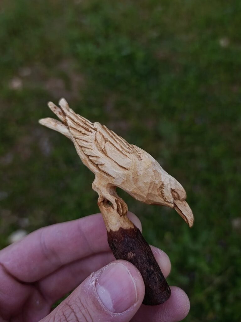 Hand-carved wooden bird perched on a small branch held by a person's hand.