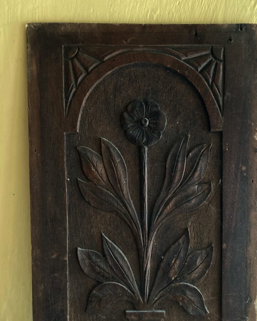 Carved wooden panel with a floral design set inside a decorative arched frame.