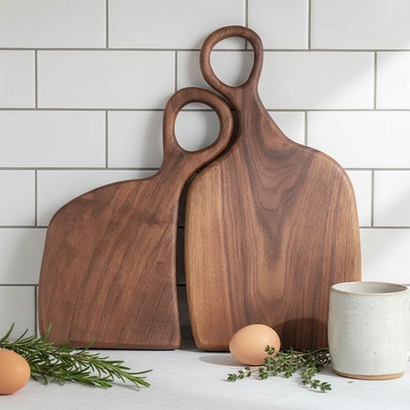 Two wooden cutting boards with handles leaning against a white tiled kitchen wall.