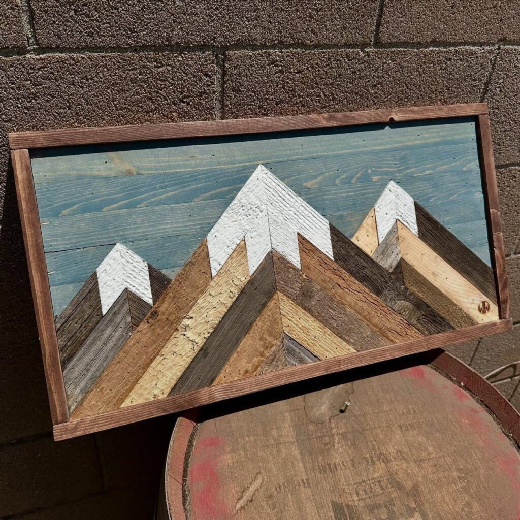 Three-dimensional wooden mountain wall art with white peaks against a blue sky background.