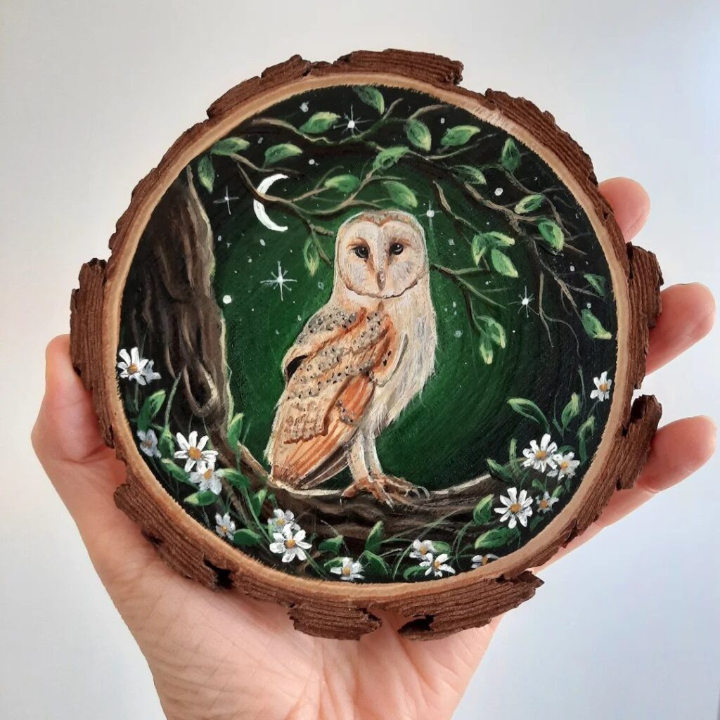 Barn owl painting on a natural wood slice held in a hand.
