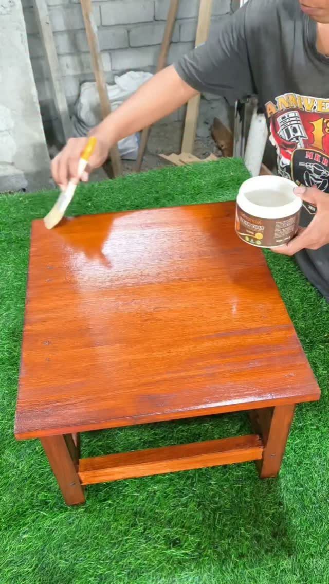 Person applying clear seal coat to a reddish-brown stained wooden table with a brush.
