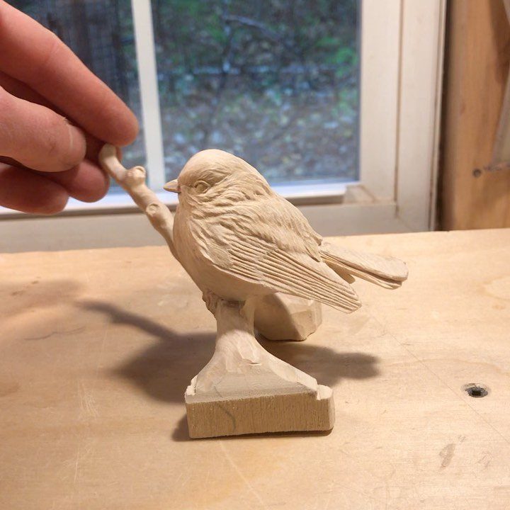 Wooden bird carving perched on a branch, held by a person's fingers.