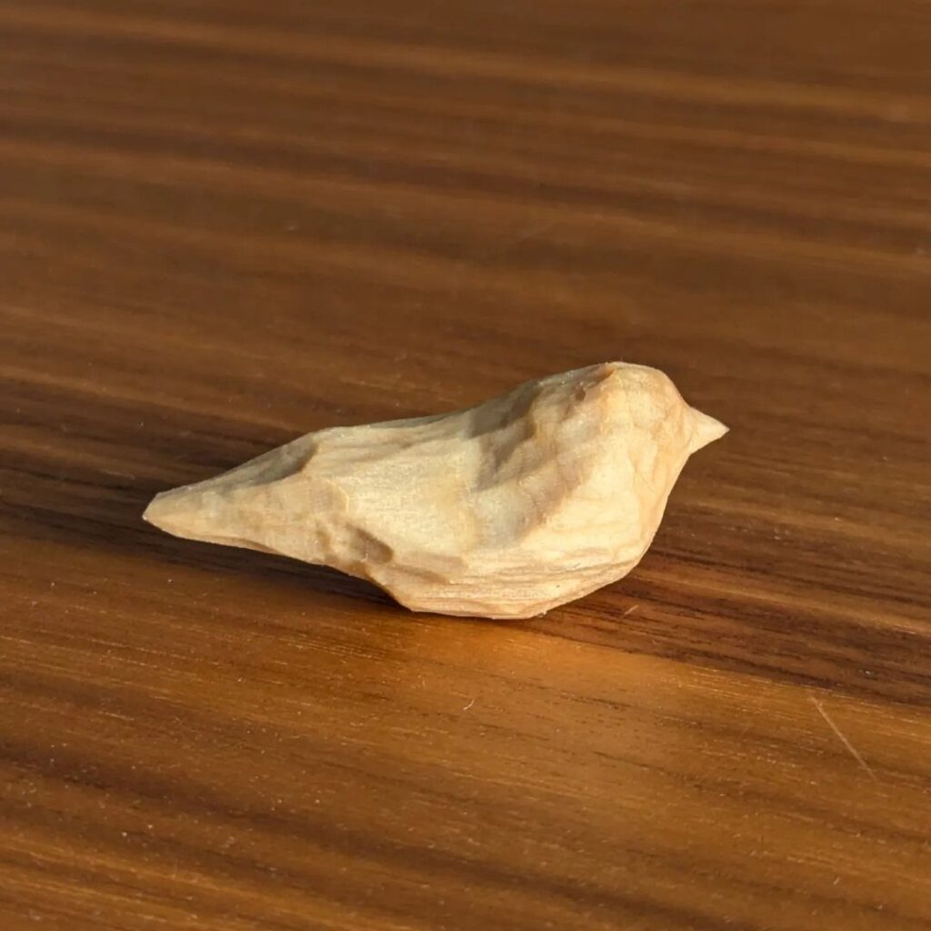 Small hand-carved wooden bird resting on a polished brown wooden tabletop