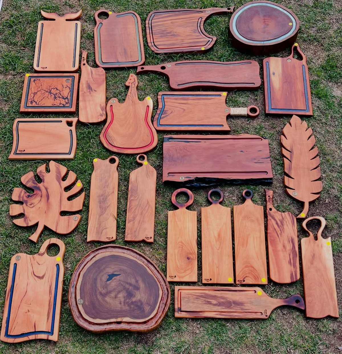 Various shaped wooden cutting boards and serving platters arranged on a green grass lawn.