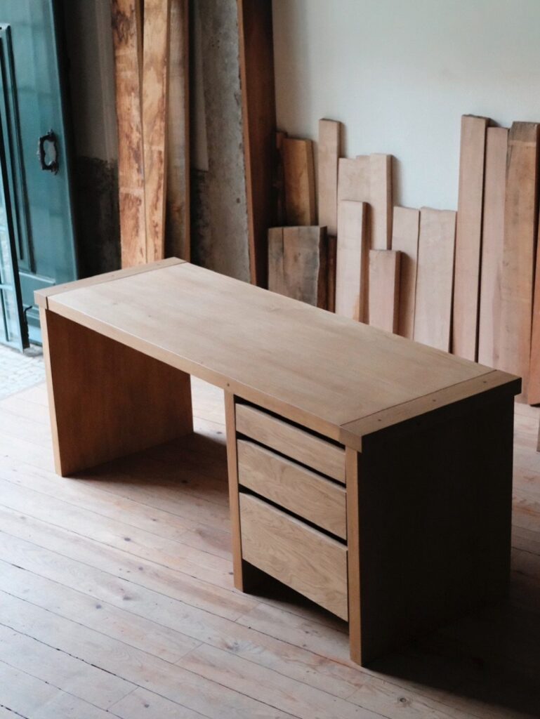 Light wooden desk with three drawers in a workshop with timber planks.