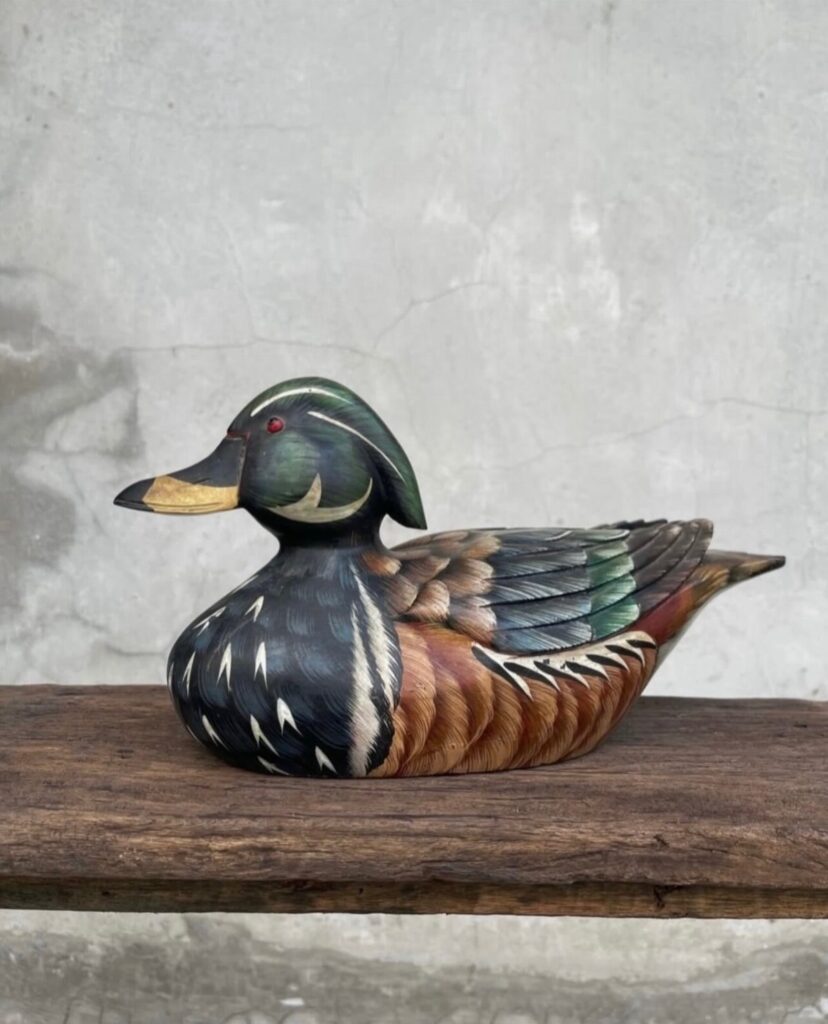 Wooden duck carving with a green head and detailed feathers on a rustic beam.