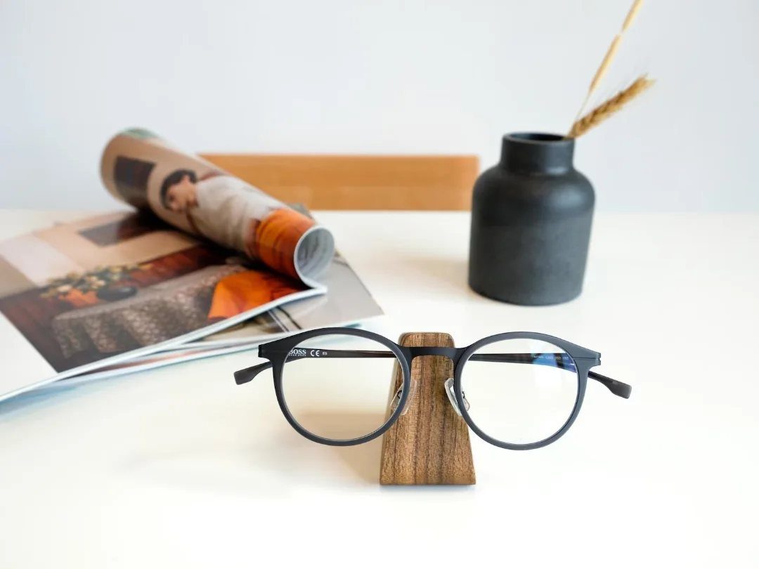 Black glasses resting on a small wooden holder on a white table