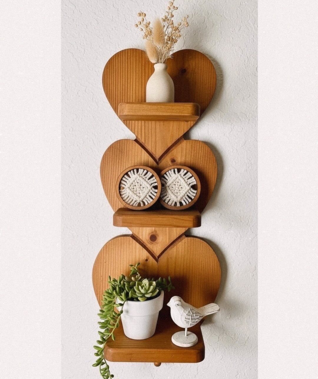 Heart-shaped wooden wall shelf decorated with a plant, vase, and bird figurine.