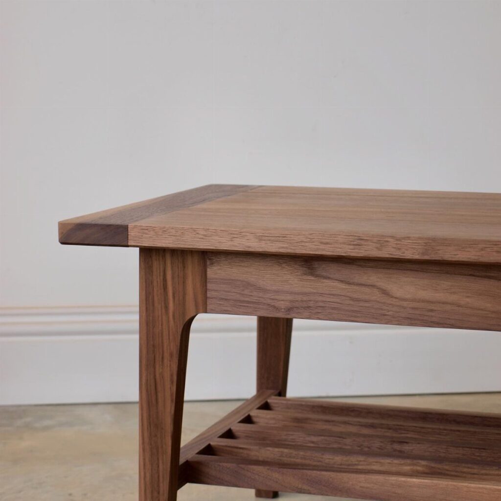 Handcrafted walnut wood coffee table with a slatted lower shelf against a white wall