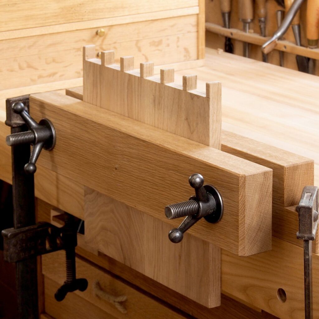 Twin-screw woodworking end vise clamping a notched piece of wood on a workbench.