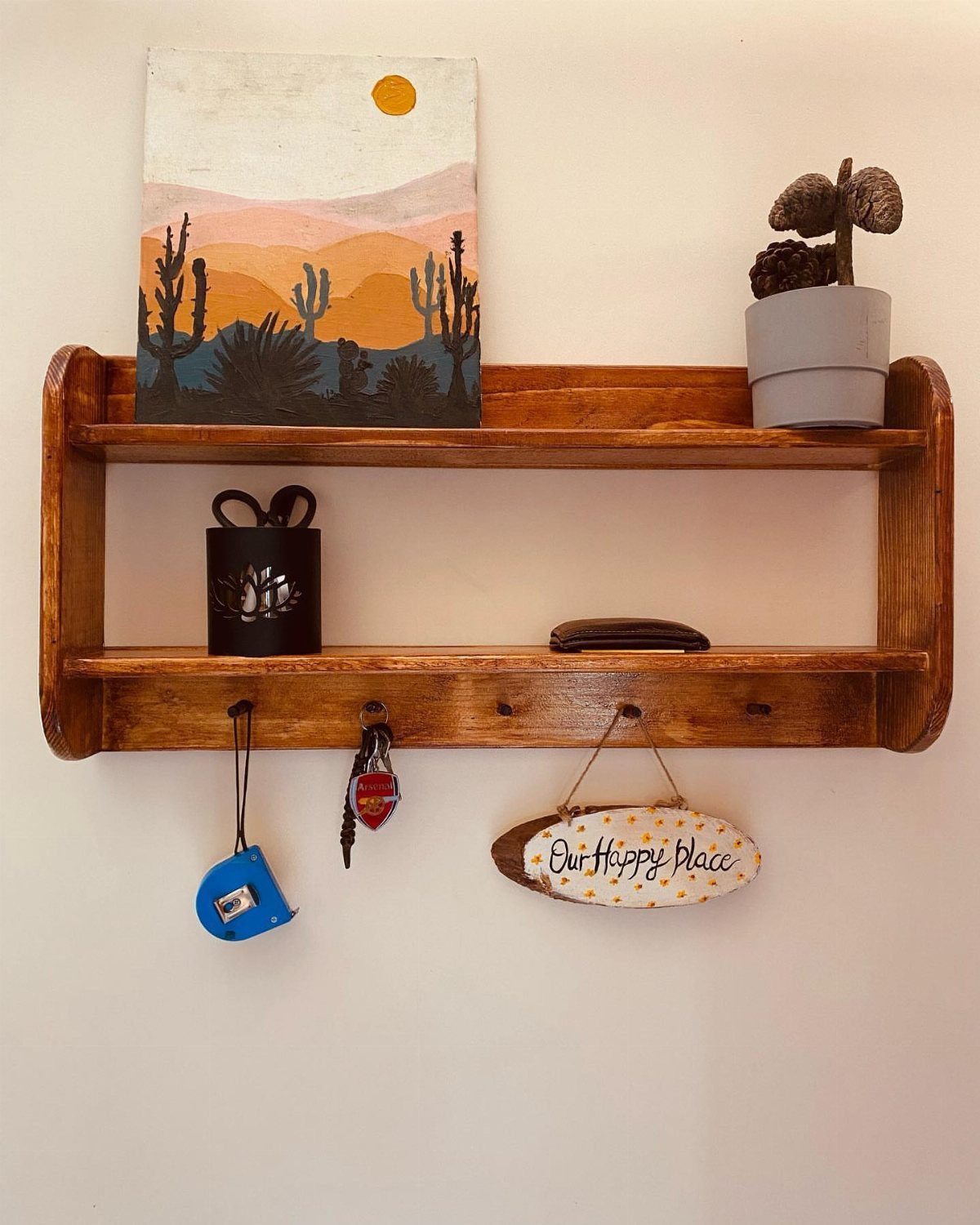 Wooden wall shelf with two tiers and hooks holding keys and home decor.